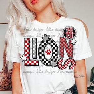以下が含まれることがあります： 赤、黒、グレーのチェック柄で「LIONS」の文字がプリントされた白いTシャツ。「O」の文字には足跡が描かれています。数字の「38」が文字の上に円で囲まれています。グレーの星が文字の周りにあります。