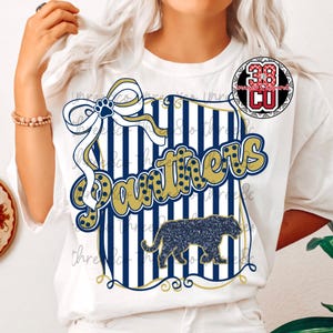Puede incluir: Camiseta blanca con un dise&ntilde;o azul marino y dorado. El dise&ntilde;o incluye la palabra "Panthers" en dorado, una silueta de pantera y un lazo con una huella de pata. La camiseta tiene cuello redondo.