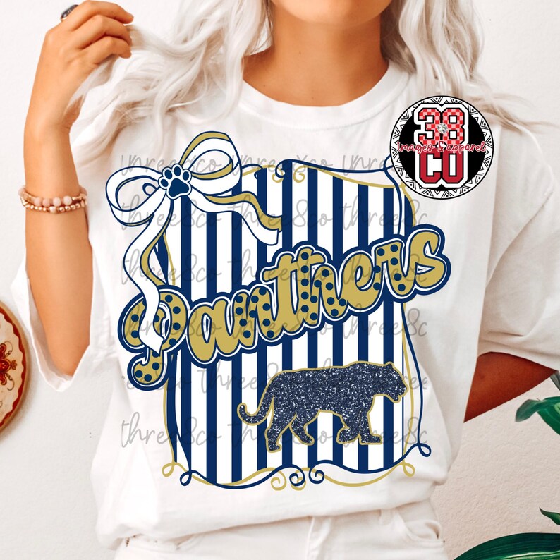 Puede incluir: Camiseta blanca con un dise&ntilde;o azul marino y dorado. El dise&ntilde;o incluye la palabra "Panthers" en dorado, una silueta de pantera y un lazo con una huella de pata. La camiseta tiene cuello redondo.