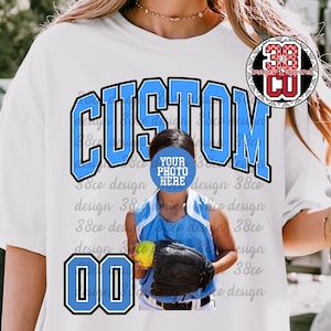 May include: White t-shirt with a blue "CUSTOM" graphic and the number "00". The shirt features a softball player in a blue uniform holding a glove and ball. The text "YOUR PHOTO HERE" is also visible.