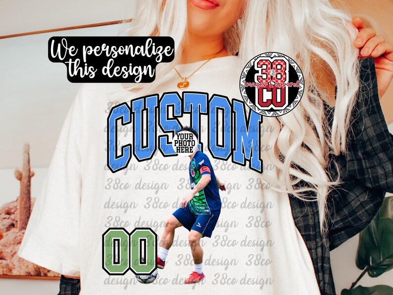 May include: Cream-colored t-shirt with the word "CUSTOM" in blue and black lettering. A soccer player graphic is featured, along with the number "00" in a green and black frame. The text "We personalize this design" is also present.