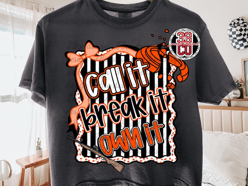 May include: Dark gray t-shirt with a graphic design that says "Call it, break it, own it." The design includes a bow, a shotgun, and a clay target. The text is in white and orange.