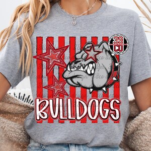 May include: A heather gray short-sleeve t-shirt featuring a graphic print of a bulldog wearing a spiked collar, two red stars, and vertical red stripes. The word BULLDOGS is printed in large white letters with a red outline at the bottom of the design.
