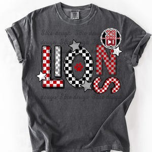 以下が含まれることがあります： 赤、白、黒のチェック柄で「LIONS」の文字が入った濃いグレーのTシャツ。「O」の文字の中央には足跡があります。「38」の数字と「CU」の文字が入った円形のパッチが「N」の文字の上にあります。