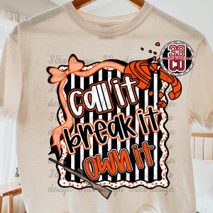 May include: Cream-colored t-shirt featuring a graphic design with the text "Call it, Break it, Own it" in white and orange. The design includes a bow, a shotgun, and a target, with black and white stripes.