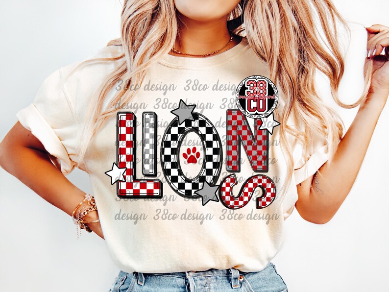 以下が含まれることがあります： 大胆なチェック柄で「LIONS」の文字がプリントされたクリーム色のTシャツ。文字は赤、黒、白で、星のアクセントが付いています。「38 CU」の円形エンブレムも表示されています。