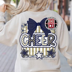 May include: Beige sweatshirt with a navy blue bow and the word "CHEER" in a checkered and striped design. The design includes three navy blue stars and a circular emblem with the number 38 and the letters CU.