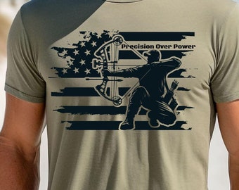 Puede incluir: Una camiseta verde con un diseño de bandera estadounidense desgastado y una silueta de un arquero con arco y flecha. El texto "Precision Over Power" está impreso en la camiseta.