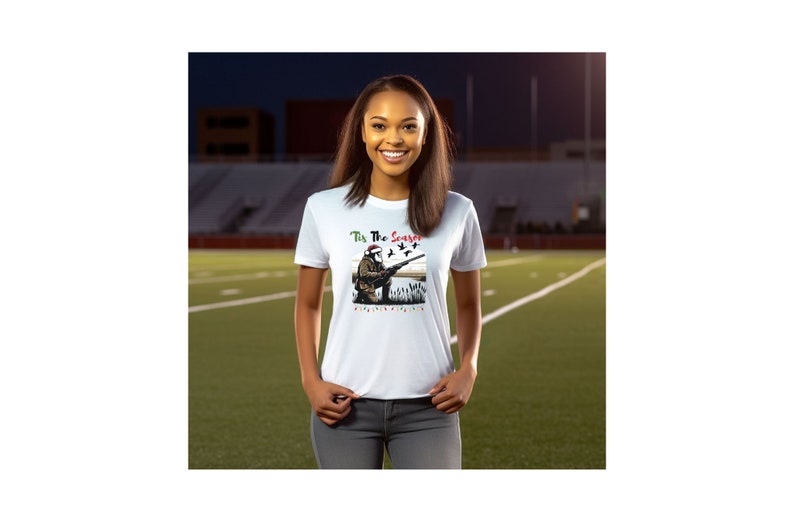 May include: White t-shirt with a Christmas-themed design featuring a hunter wearing a Santa hat and holding a shotgun, with the text "Tis The Season" above the image.