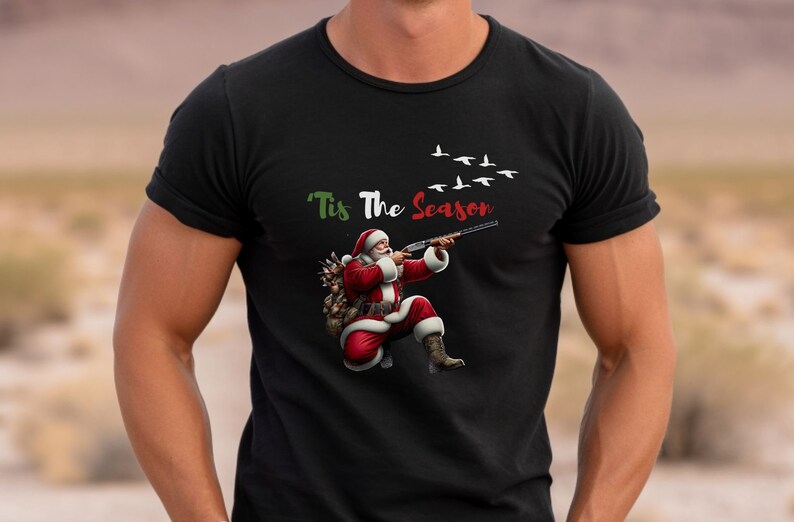 May include: Black t-shirt featuring Santa Claus aiming a shotgun, with the text "'Tis The Season" above. Santa is dressed in his traditional red suit and boots, with a sack of gifts. White birds fly in the background.