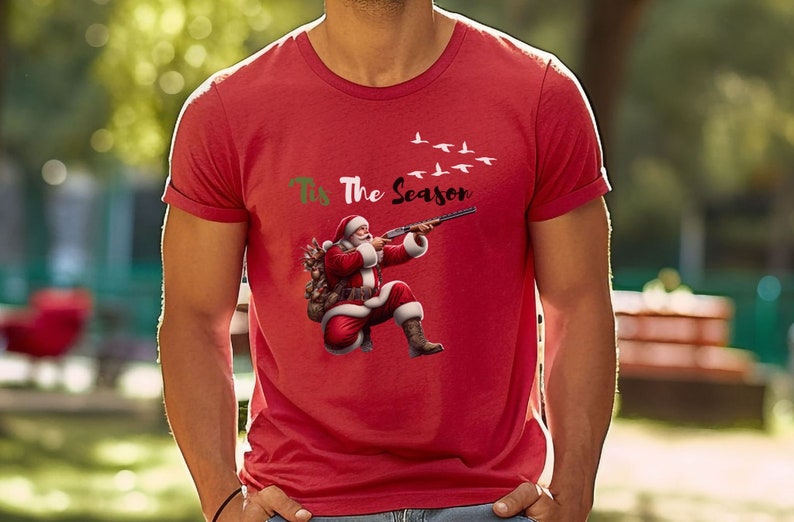 May include: Red t-shirt featuring Santa Claus aiming a shotgun at flying birds. The phrase "Tis The Season" is printed above the Santa illustration. A festive and humorous design for the holiday season.