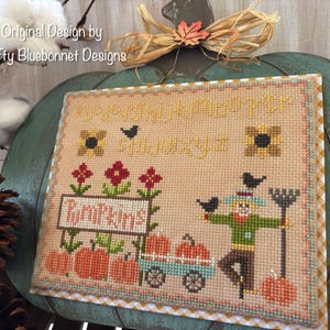 May include: Cross stitch pattern featuring a scarecrow, pumpkins, sunflowers, and birds. The text reads "It's the little things that make life so happy".