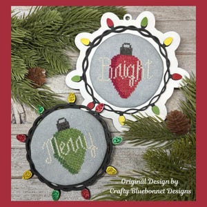 May include: Two Christmas ornaments with cross-stitched bulb designs. One ornament features a red bulb with the word "Enlight" and the other has a green bulb with the word "Noel". Both are surrounded by a string of colorful lights and set against a backdrop of pine needles.