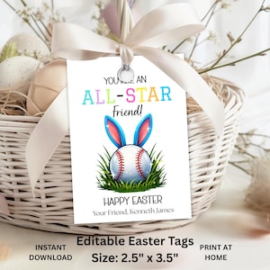 Puede incluir: Una etiqueta de regalo blanca con el texto "YOU ARE AN ALL-STAR Friend!" y "HAPPY EASTER". La etiqueta presenta una pelota de béisbol con orejas de conejo y mide 6,35 cm x 8,89 cm. La etiqueta está sujeta a una cesta con un lazo blanco.