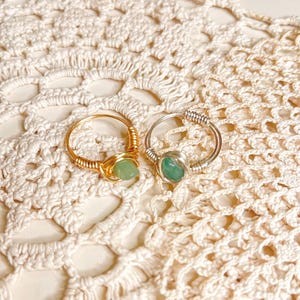 May include: Two wire-wrapped rings with green gemstone accents. One ring is gold and the other is silver.