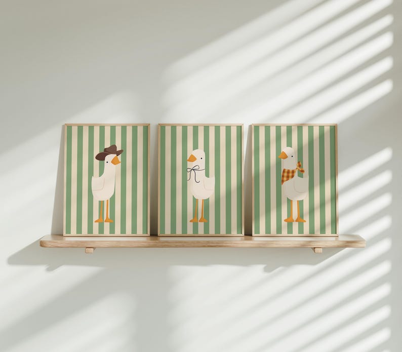 May include: Three framed prints with green and white striped backgrounds and illustrations of geese. The geese are wearing different accessories, including a cowboy hat, a bow, and a scarf.