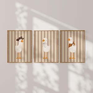 May include: Three framed prints with a striped background. Each print features a white goose with different accessories. The first goose is wearing a cowboy hat, the second goose is wearing a bow, and the third goose is wearing a scarf.