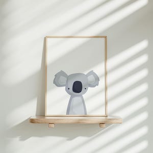 Puede incluir: Una impresi&oacute;n enmarcada de un koala de dibujos animados con un fondo gris claro. El koala est&aacute; de frente con las orejas levantadas y los brazos a los lados. El marco es de madera clara.