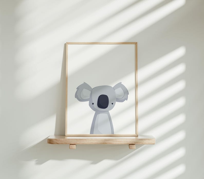 Puede incluir: Una impresi&oacute;n enmarcada de un koala de dibujos animados con un fondo gris claro. El koala est&aacute; de frente con las orejas levantadas y los brazos a los lados. El marco es de madera clara.