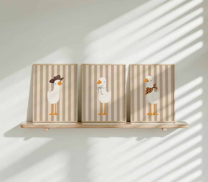 May include: Three framed prints with a striped background and illustrations of geese. The geese are wearing different accessories, including a cowboy hat, a bow, and a scarf.