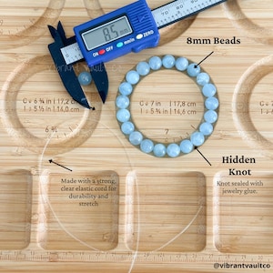 K&ouml;nnte beinhalten: Ein hellblaues Perlenarmband mit 8 mm Perlen. Das Armband wird mit einem digitalen Messschieber mit 8,5 mm gemessen. Der Text lautet: "Hergestellt mit einer starken, transparenten elastischen Schnur f&uuml;r Haltbarkeit und Dehnung."