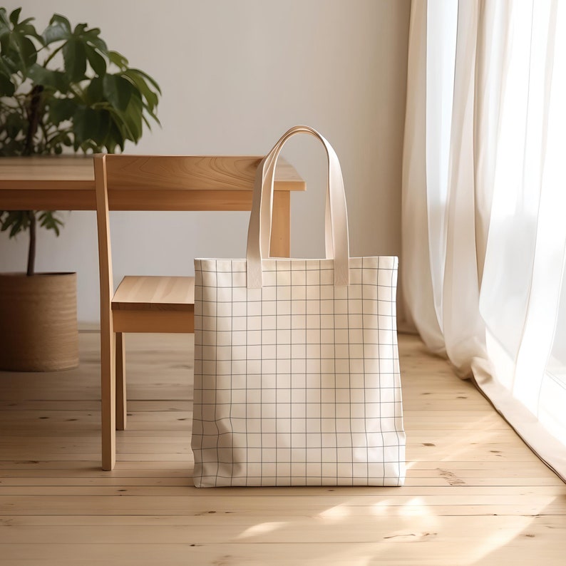 Puede incluir: Una bolsa de lona blanca con un patr&oacute;n de cuadr&iacute;cula negra. La bolsa tiene dos asas y est&aacute; sentada en un suelo de madera.