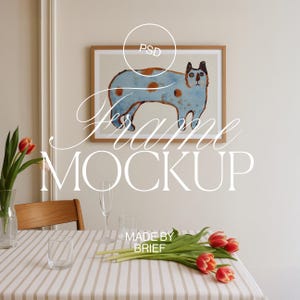 Pode incluir: Uma ilustração enquadrada de um gato azul com manchas marrons e olhos pretos. O quadro está em uma parede branca acima de uma mesa com uma toalha de mesa listrada, um vaso de tulipas e dois copos.