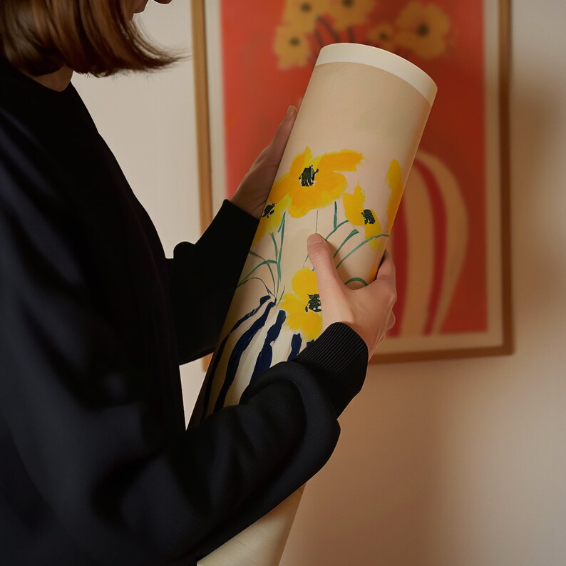 Puede incluir: Una persona sostiene un estampado enrollado de un ramo de flores amarillas sobre un fondo crema. El estampado est&aacute; en un tubo con la parte superior e inferior blancas.