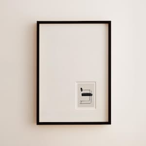 May include: A framed art print featuring a minimalist illustration of a black chair with a rectangular seat and curved armrest. The print is set against a cream-colored background within a black frame, creating a modern aesthetic.