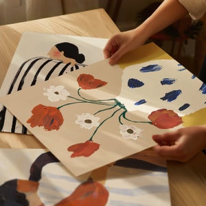 May include: A beige canvas print with a stylized illustration of a bouquet of red and white flowers in a blue and white patterned vase. The flowers are painted in a loose, abstract style.
