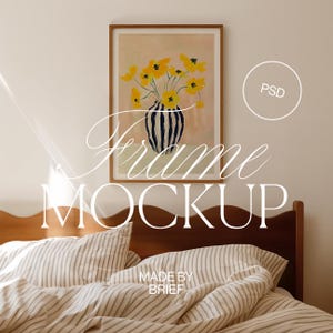 Könnte beinhalten: Ein gerahmter Druck eines gelben Blumenarrangements in einer schwarz-weiß gestreiften Vase vor einem hellrosa Hintergrund. Der Rahmen hängt an einer weißen Wand über einem Holz-Kopfteil mit einer gestreiften Bettdecke.