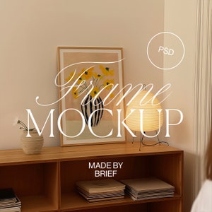 Puede incluir: Una impresión artística enmarcada con flores amarillas en un jarrón a rayas. La obra de arte se exhibe en un mueble de madera, junto a una lámpara de papel y un pequeño jarrón con una flor blanca. El texto "Frame Mockup" está superpuesto.