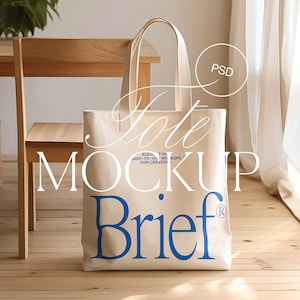 Könnte beinhalten: Ein beigefarbener Canvas-Tote-Bag-Mockup mit dem Text "tote mockup" und "Brief" in blauer Schrift. Die Tasche liegt auf einer Holzoberfläche.
