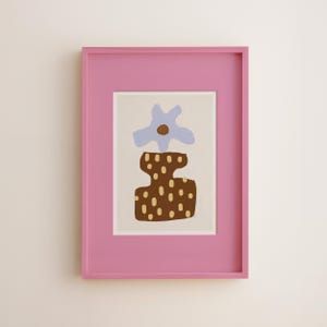 May include: A framed art print featuring an abstract floral design. The artwork has a light blue flower and a brown vase with tan dots. The frame is a bright pink color, adding a pop of color to the piece.