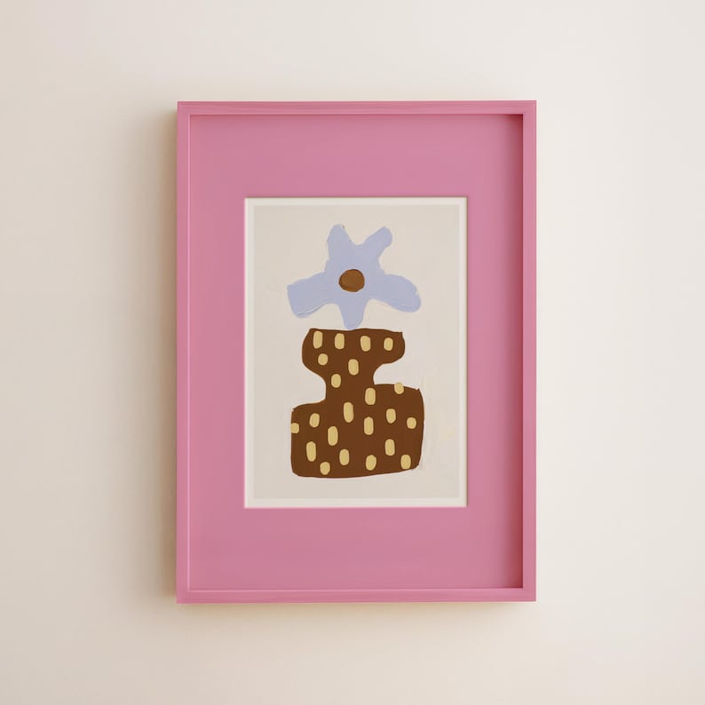 May include: A framed art print featuring an abstract floral design. The artwork has a light blue flower and a brown vase with tan dots. The frame is a bright pink color, adding a pop of color to the piece.
