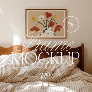 Op de afbeelding: Een ingelijste illustratie van een boeket rode en witte bloemen in een witte vaas met zwarte stippen. De lijst is van bruin hout en de illustratie is op een beige achtergrond. De lijst hangt aan een witte muur boven een bed met een wit en beige gestreept dekbed.