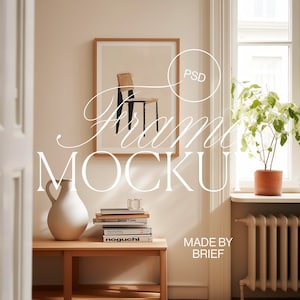 Puede incluir: Una impresión enmarcada de una silla de estilo minimalista, colgada en una pared beige. El marco es de madera y tiene un acabado marrón claro. La impresión es en blanco y negro y muestra una silla con un diseño simple. El marco está colgado en una pared con una moldura blanca. Hay libros y un jarrón sobre una mesa de madera delante del marco. El texto "Frame Mockup" está superpuesto a la imagen. El texto "Made by Brief" está en la esquina inferior derecha de la imagen.
