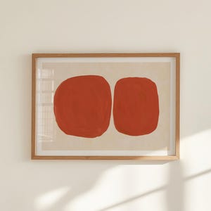 K&ouml;nnte beinhalten: Abstrakter Kunstdruck mit zwei gro&szlig;en, roten, organischen Formen auf cremefarbenem Hintergrund. Das Kunstwerk ist in einem hellbraunen Holzrahmen gerahmt. Eine moderne Wanddekoration, passend f&uuml;r verschiedene Einrichtungsstile.