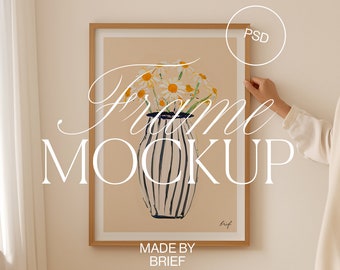 May include: A framed art print showing a vase of daisies. The vase has vertical black and white stripes. The frame is light brown. The words "Frame Mockup" and "Made by Brief" are visible on the print.