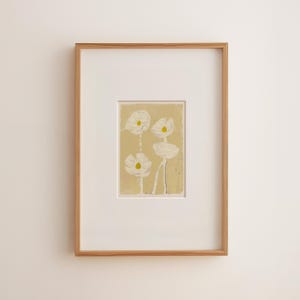 May include: A framed art print featuring four white flowers with yellow centers against a light yellow background. The artwork is encased in a white mat and a natural wood frame, creating a minimalist aesthetic.