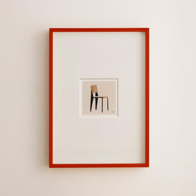 May include: A framed art print featuring a minimalist illustration of a chair. The chair has a light brown back and seat with black legs. The artwork is set within a white mat and a vibrant red frame.