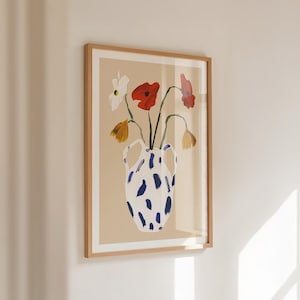 May include: A framed art print featuring a watercolor painting of flowers in a vase. The vase is white with blue brushstrokes. The flowers are red, white, and yellow. The artwork is framed in a light brown wooden frame.