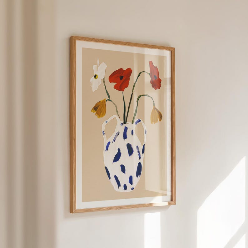 May include: A framed art print featuring a watercolor painting of flowers in a vase. The vase is white with blue brushstrokes. The flowers are red, white, and yellow. The artwork is framed in a light brown wooden frame.