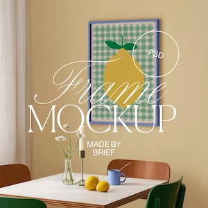 Może przedstawiać: Oprawiony wydruk artystyczny z ilustracją żółtej cytryny na zielono-białym tle w kratkę. Rama jest niebieska. Słowa "Frame MOCKUP" są wyświetlane ozdobną czcionką. Stół jest nakryty cytrynami, niebieskim kubkiem i wazonem z kwiatami.