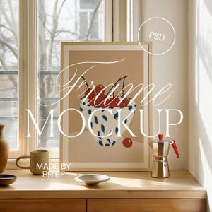 May include: A framed print of a bowl of red cherries with a blue and white pattern. The frame is on a wooden table with a coffee pot, a mug, and a small bowl.