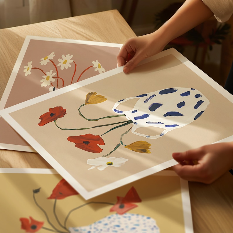 May include: A set of three prints featuring floral arrangements in a blue and white patterned vase. The prints are on a beige background and feature red poppies, yellow flowers, and white flowers.