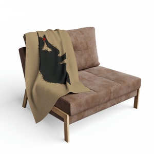 Puede incluir: Un sofá de ante marrón con una manta de tiro que presenta una silueta negra de un elefante con un corazón rojo en su trompa.