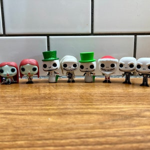 Op de afbeelding: Een verzameling van negen Nightmare Before Christmas Pop-figuren. De figuren omvatten Jack Skellington, Sally, Oogie Boogie en Zero. De figuren staan allemaal in hun kenmerkende poses en zijn gemaakt van vinyl.