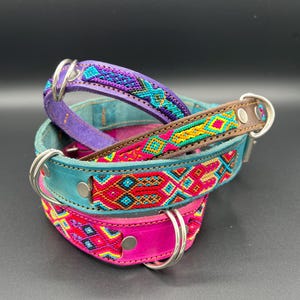 May include: Three colorful dog collars stacked on top of each other. The collars are made of leather and feature intricate woven patterns in shades of purple, teal, pink, red, and yellow. Each collar has a silver metal ring for attaching a leash.
