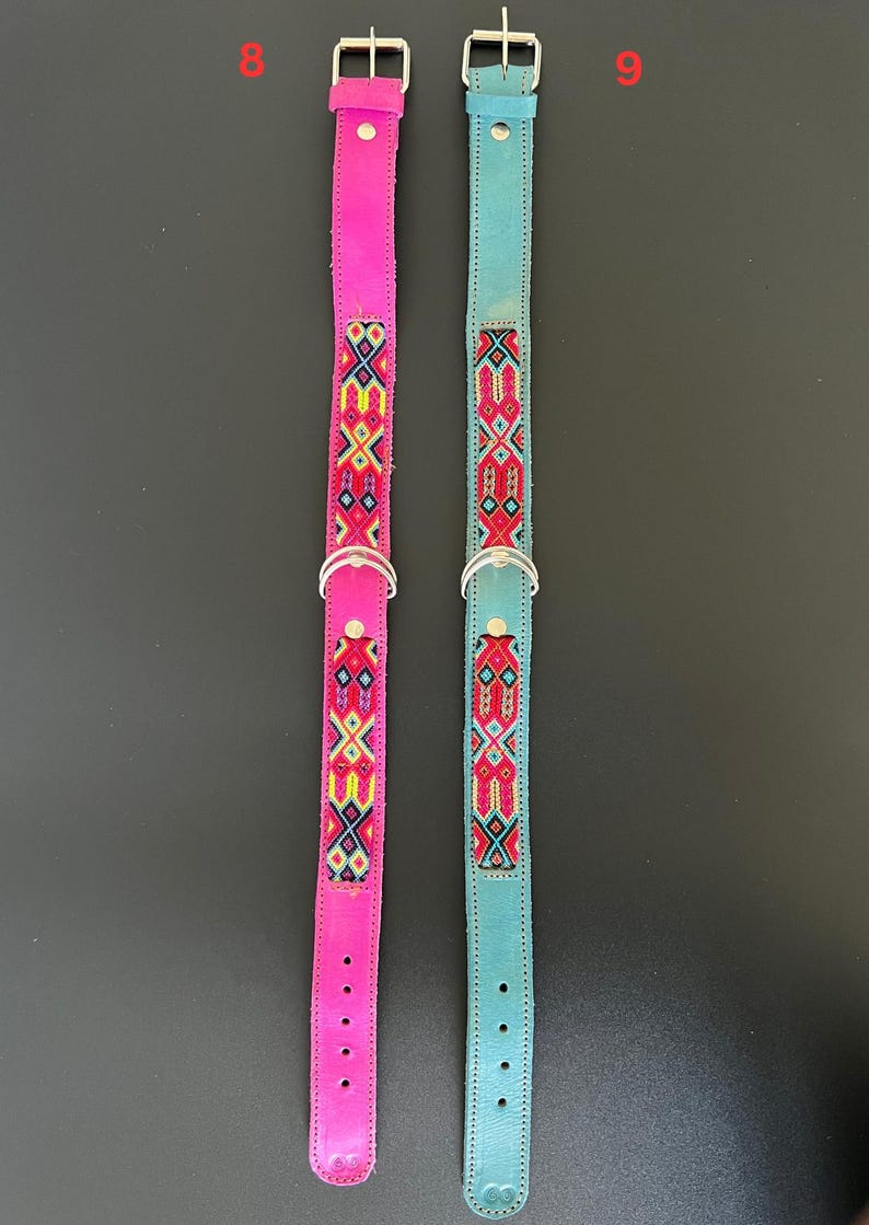 May include: Two dog collars. One is bright pink, the other is teal. Both have a silver metal buckle and a D-ring. The collars are decorated with a colorful embroidered pattern in red, yellow, and blue. The collars are made of leather.